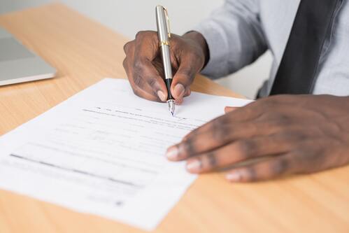 A person's hand holding a pen signing a contract | Collection Services Michigan