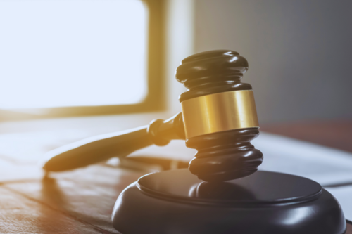Photo of a gavel laying on a desk lit by a window in the background.